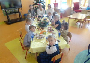 Pani dyrektor Maria Królikowska, pani Ania Tylman oraz dzieci jedzą słodki i owocowy poczęstunek.
